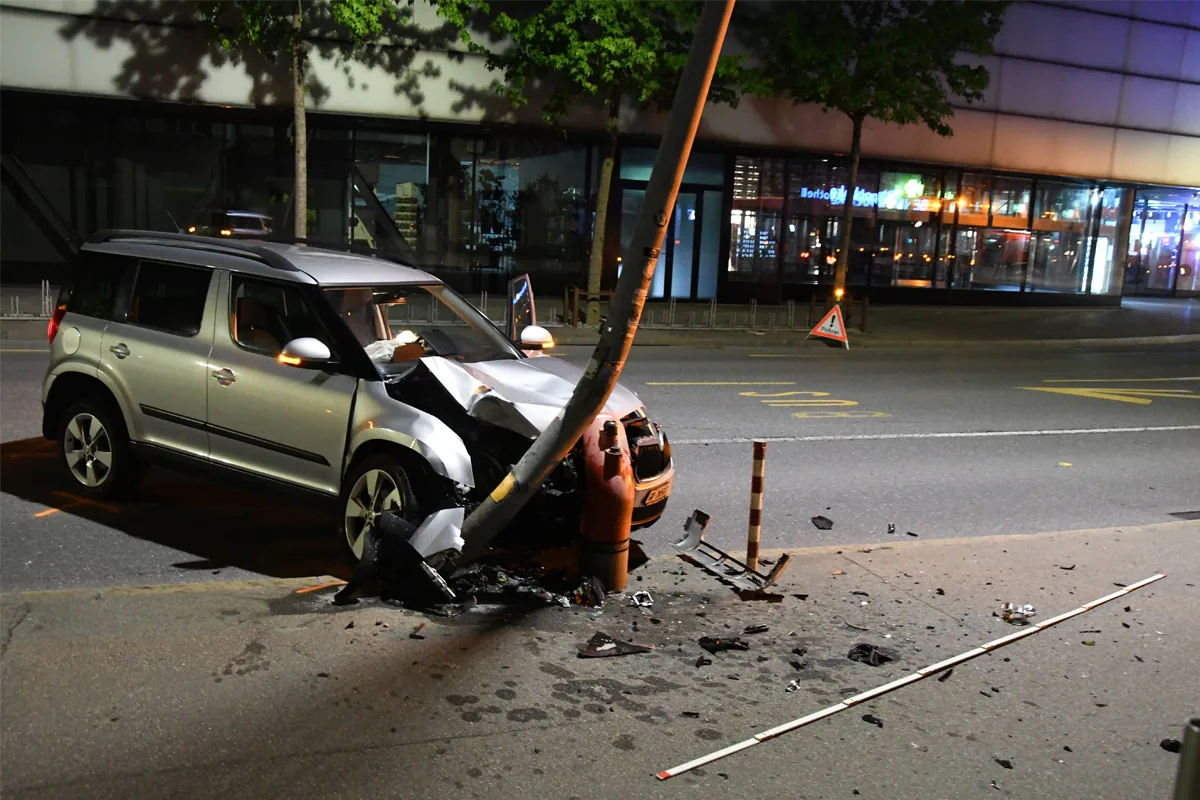 Ein silberfarbenes Auto ist bei Nacht gegen einen Laternenmast gefahren. Der Mast ist stark geneigt, das Auto weist erhebliche Frontschäden auf.