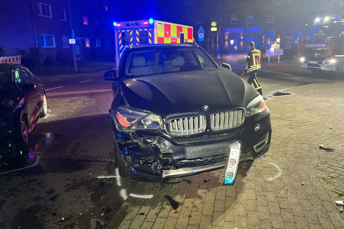 Ein schwarzer BMW mit Beschädigungen an der Front steht bei Nacht auf einer Straße. Im Hintergrund ist ein Rettungsfahrzeug zu sehen.