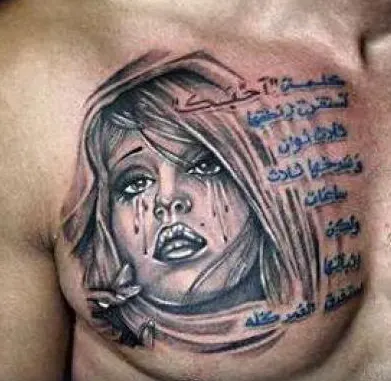 Ein Tattoo zeigt ein weinendes Gesicht mit verlaufendem Make-up und arabischem Text auf einer männlichen Brust.