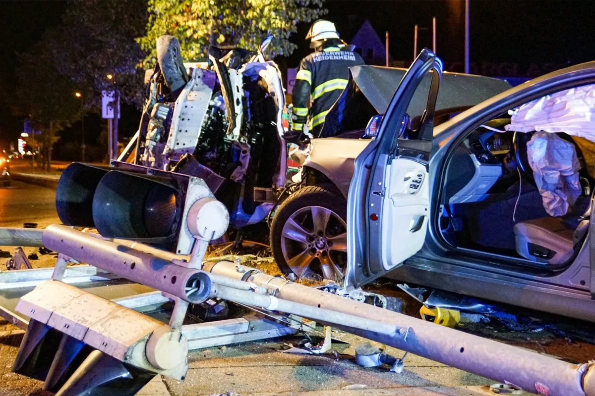 Ein stark beschädigtes Auto mit geöffneten Türen und ausgelösten Airbags steht neben einer umgekippten Ampel. Ein Feuerwehrmann ist im Hintergrund zu sehen.