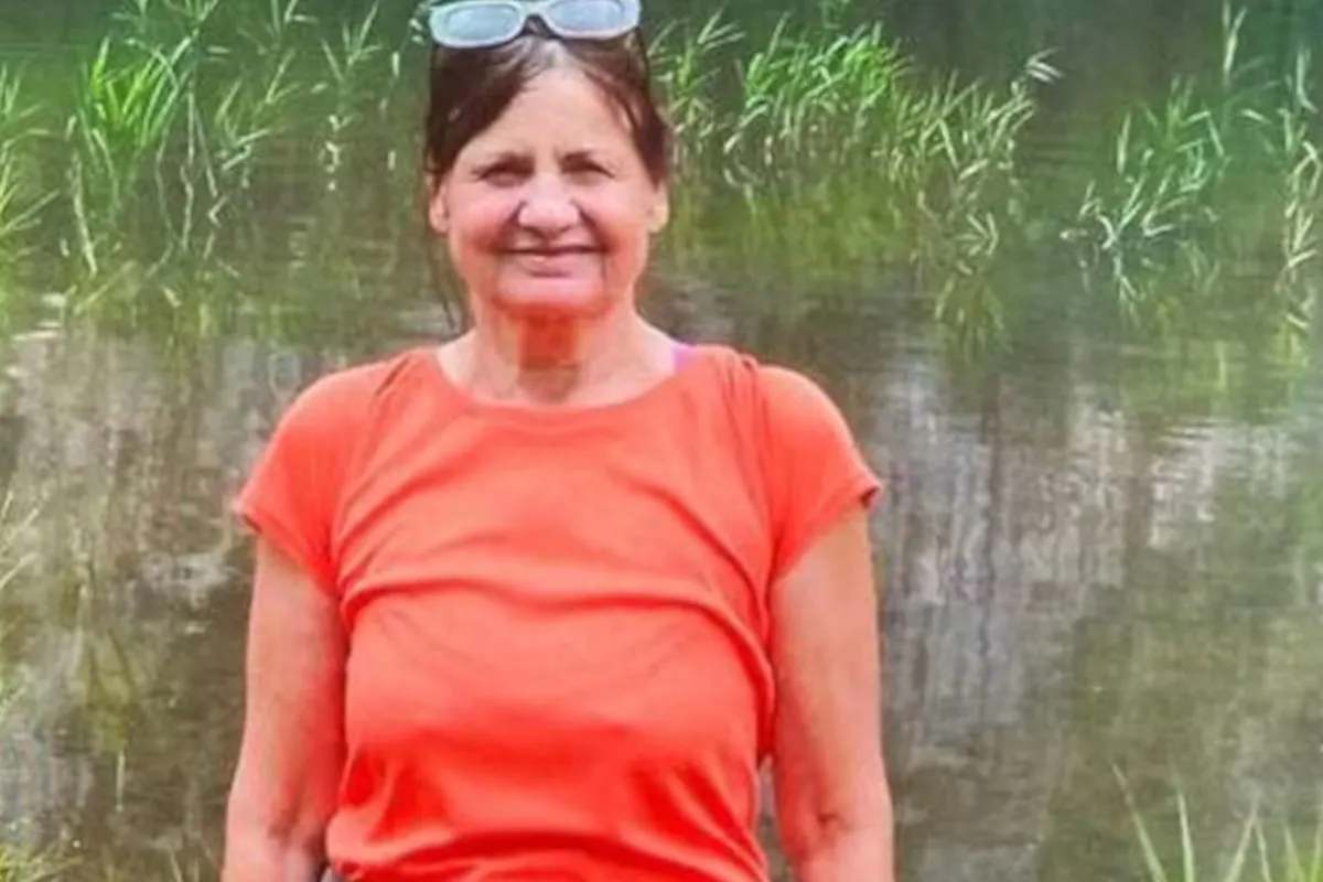 Eine Frau mit dunklen Haaren und einem orangen T-Shirt steht vor einem Teich mit grüner Vegetation.