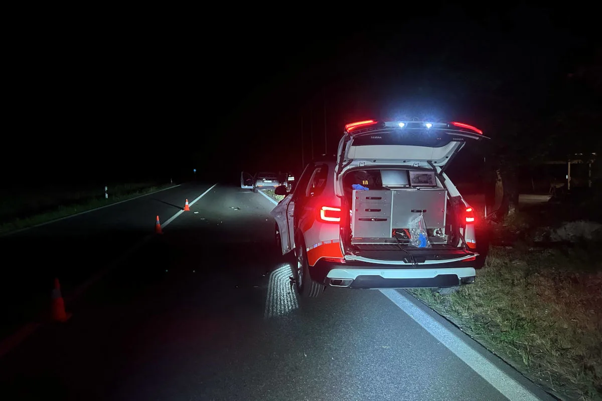 Ein Einsatzfahrzeug mit geöffnetem Kofferraum steht auf einer dunklen Landstraße. Warnkegel markieren die Fahrbahn.
