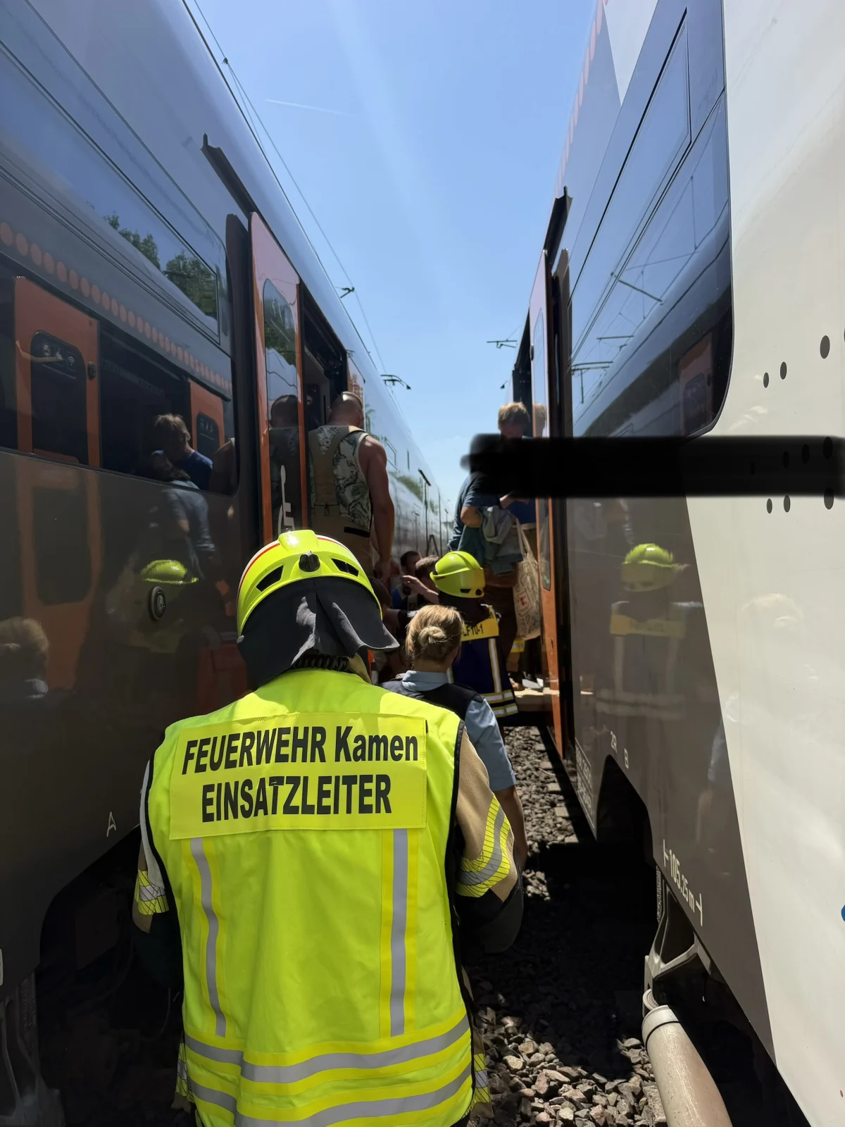 Ein Feuerwehrmann der Feuerwehr Kamen steht zwischen zwei Zügen; Personen werden aus den Zügen evakuiert.