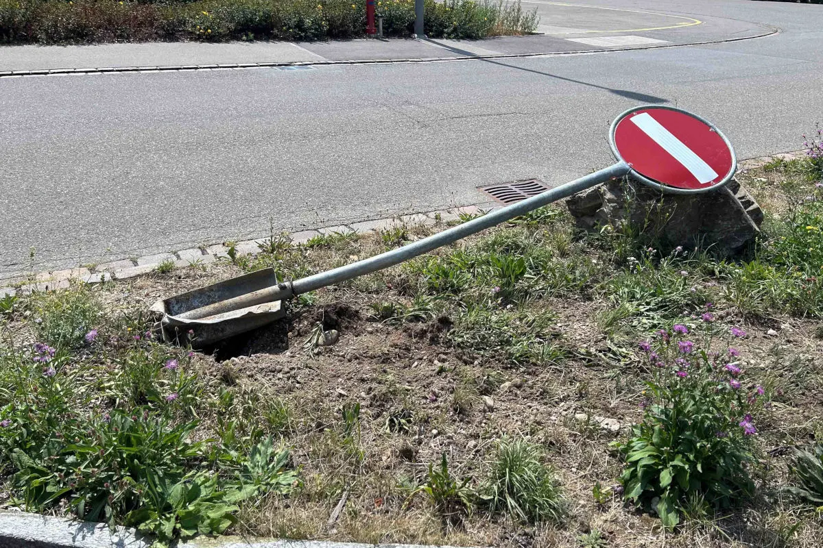 Ein Einfahrverbotsschild liegt umgekippt auf einer Grünfläche neben einer asphaltierten Straße. Das Schild ist verbogen und zeigt eine deutliche Beschädigung.