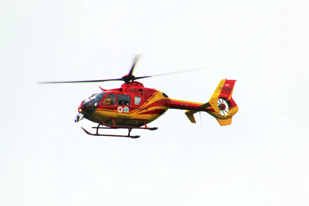 Ein rot-gelber Rettungshubschrauber mit der Aufschrift 'Notarzt' fliegt am Himmel, auf der weißen Fläche sichtbar.