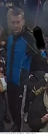 Ein Mann mit blauer Jacke steht in einer Menschenmenge. Er wird von einer Überwachungskamera erfasst.