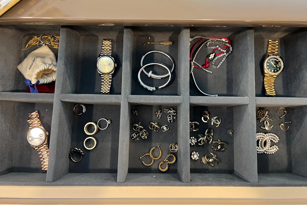 In einer offenen Schatulle befinden sich mehrere Fächer, die mit Uhren, Armbändern und Ohrringen gefüllt sind. Die Stücke wirken hochwertig und luxuriös.