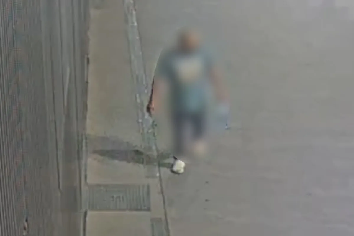 Eine unkenntliche Person läuft entlang eines grauen Gehwegs an einer hohen Betonwand, aufgenommen von einer Überwachungskamera.