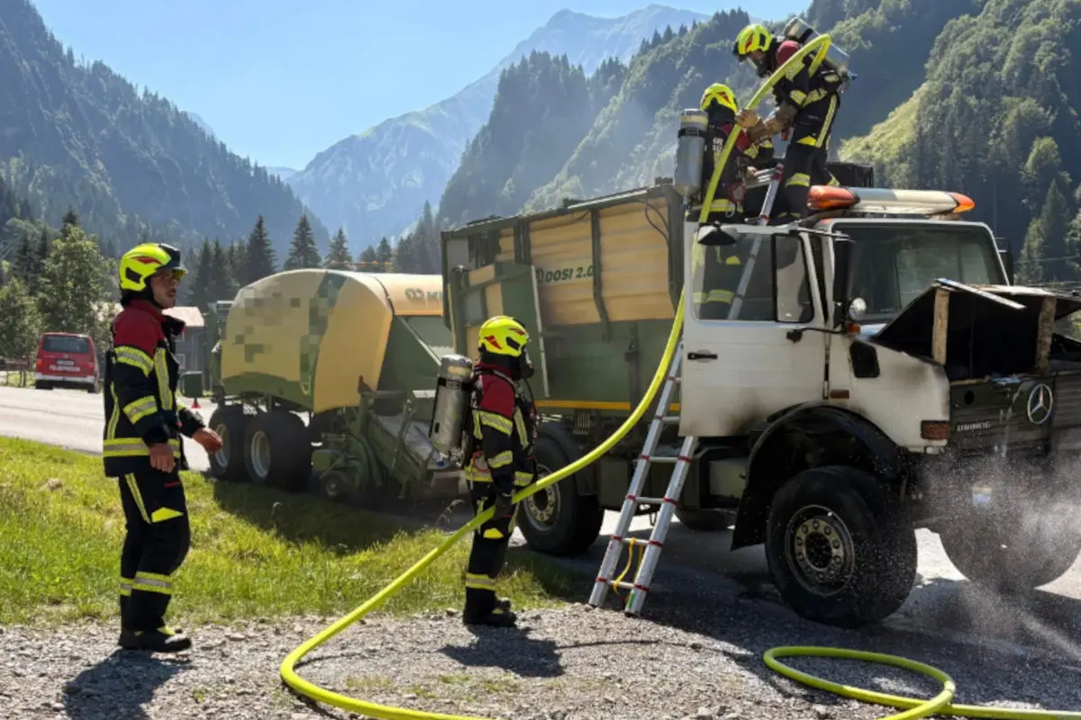 Mehrere Feuerwehrleute in Schutzkleidung arbeiten in alpiner Umgebung auf einem LKW mit angelehnter Leiter und Wasserleitung.