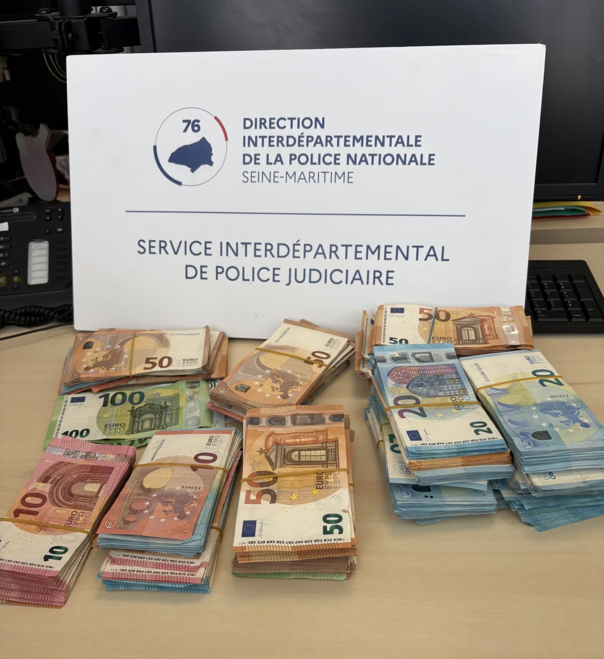 Stapel von Euro-Geldscheinen liegen auf einem Tisch vor einem Schild der Polizei Nationale Seine-Maritime.