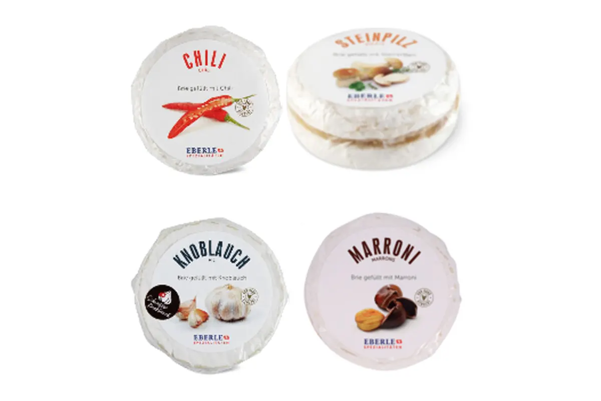 Das Bild zeigt vier verpackte Briekäse-Sorten: Chili, Steinpilz, Knoblauch und Marroni. Jede Packung hat eine Abbildung des Hauptinzg.
