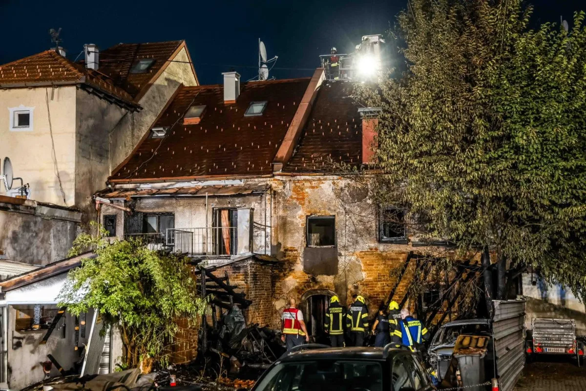 Ein stark beschädigtes Wohnhaus steht nachts im Mittelpunkt der Szene, umgeben von Einsatzkräften, die das Gebäude inspizieren.