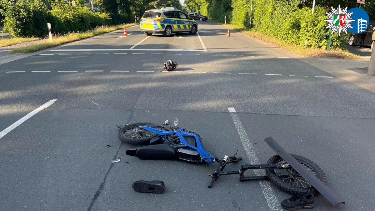 Ein verunglücktes Fahrrad mit abgetrenntem Vorderrad liegt auf einer Straße. Im Hintergrund steht ein Polizeiwagen.