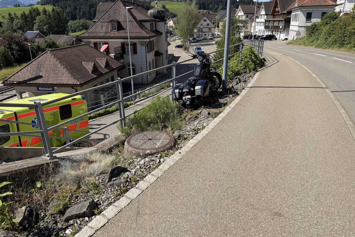 Ein Motorrad steht gegen ein Geländer gelehnt auf einem Bürgersteig neben der Straße in Waldstatt. Daneben ist ein Notarztwagen zu sehen.