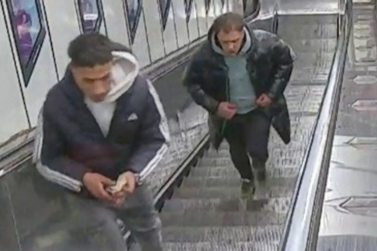 Zwei Männer werden beim Betreten einer Rolltreppe in einer U-Bahn-Station von einer Überwachungskamera aufgenommen. Einer der Männer hält etwas in den Händen.