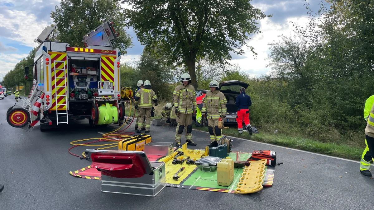Mehrere Feuerwehrleute in voller Montur stehen neben einem Einsatzfahrzeug auf einer Straße. Diverse Ausrüstungsgegenstände sind auf der Straße ausgebreitet.