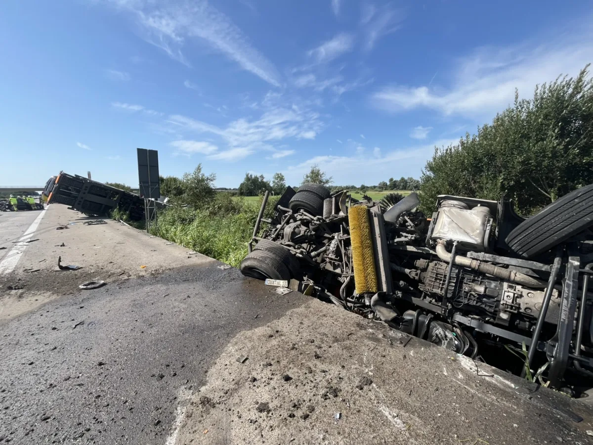 Ein Lastwagen liegt umgestürzt im Straßengraben neben einer Autobahn. Trümmerteile sind auf der Fahrbahn verstreut.