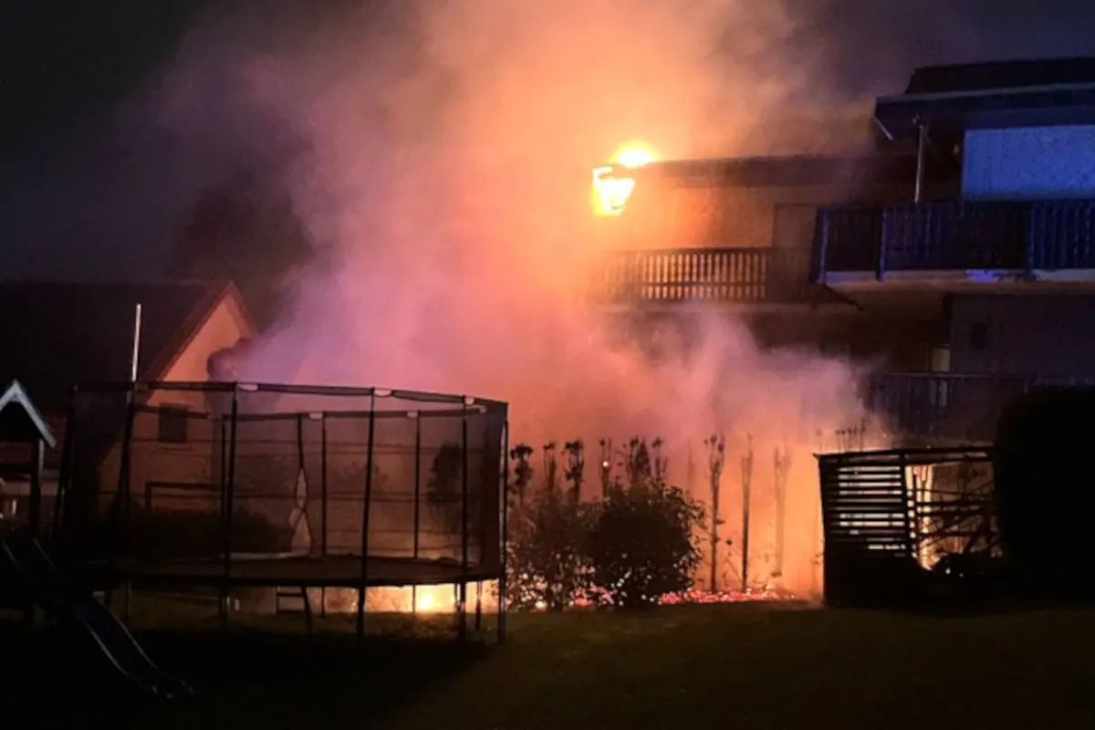 Ein Haus steht nachts in Flammen, umgeben von dichtem Rauch. Das Feuer scheint aus einem oberen Bereich des Gebäudes zu kommen.