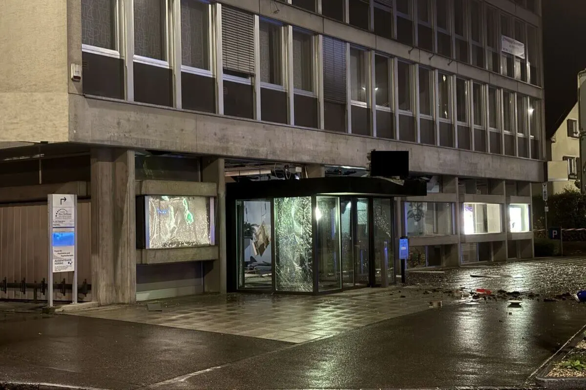 Ein Gebäude mit einem zerbrochenen Glaseingang, umgeben von reflektierendem, nassem Boden bei Nacht.