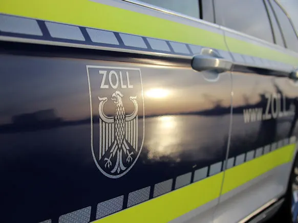 Ein Zollfahrzeug mit einem auffälligen Emblem ist bei Sonnenuntergang zu sehen. Die Seite des Fahrzeugs spiegelt das Licht.