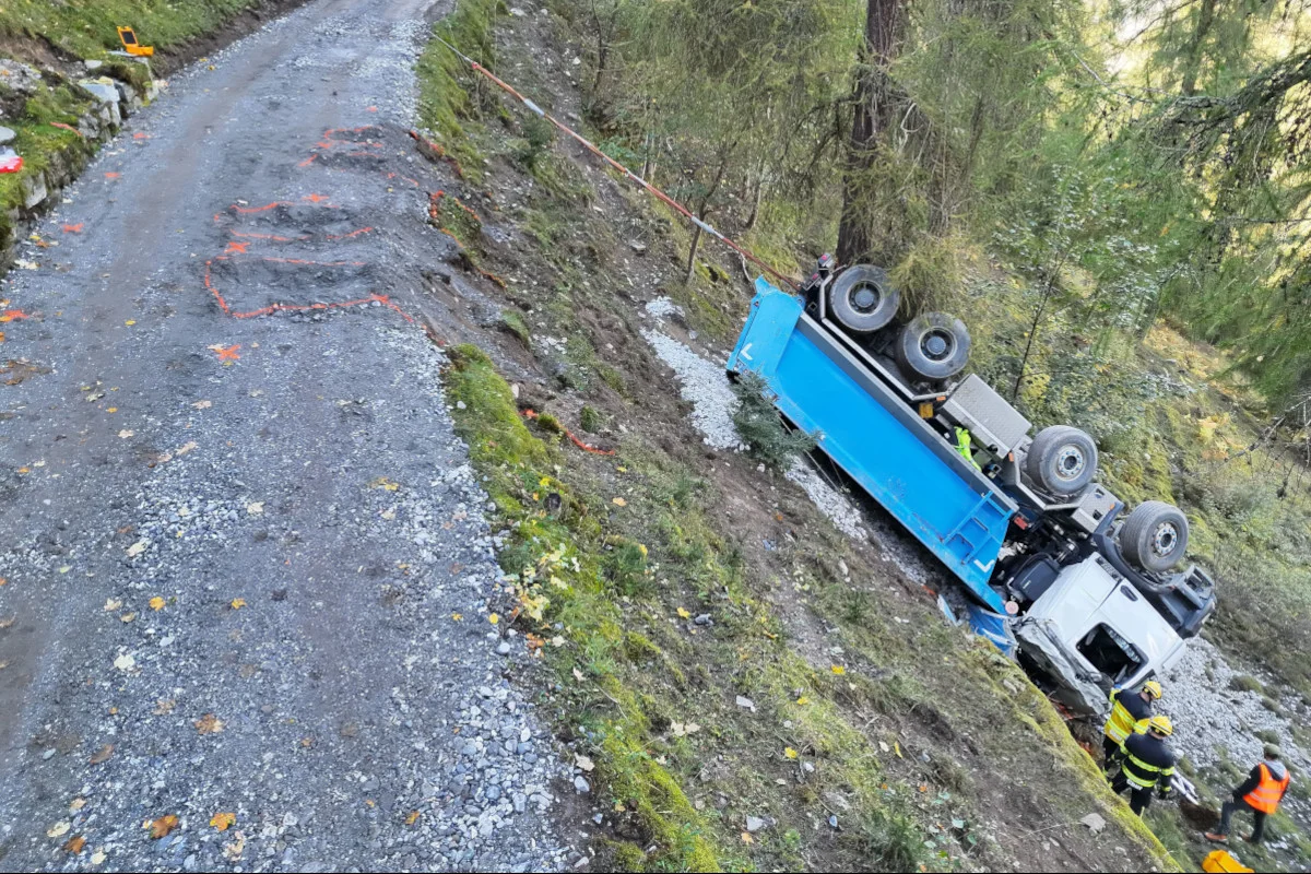 Ein blauer Lastwagen liegt umgekippt neben einer Waldstraße. Einsatzkräfte sind vor Ort, um die Situation zu sichern.