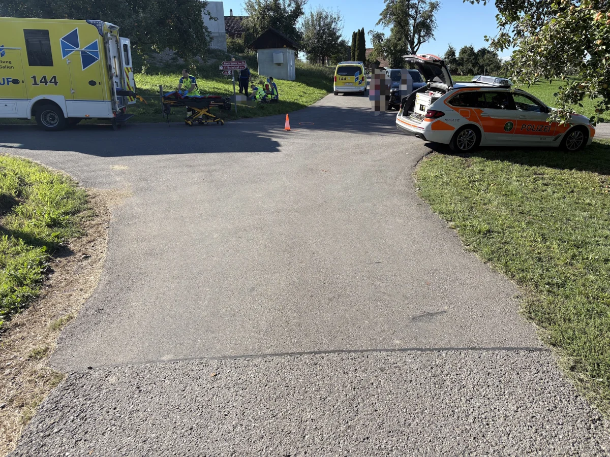Mehrere Einsatzfahrzeuge, darunter ein Krankenwagen und ein Polizeiwagen, stehen an einer Unfallstelle auf einer ländlichen Straße. Rettungskräfte sind vor Ort und das Wetter ist sonnig.