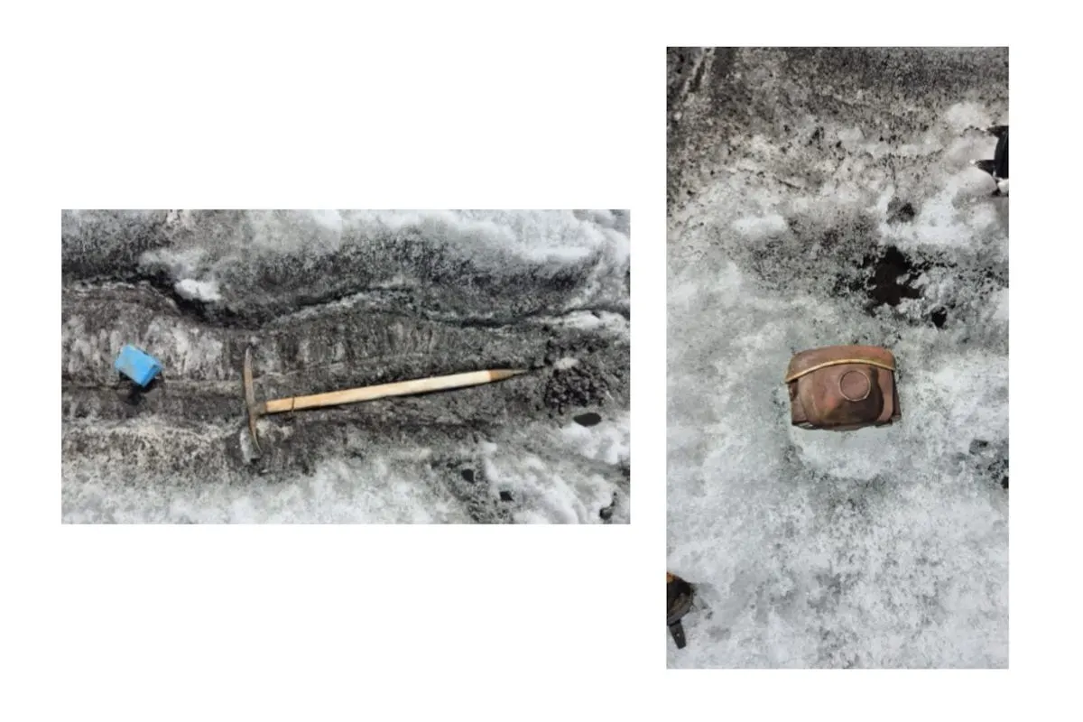 Ein Eisbeil liegt auf einer dunklen Schneefläche; daneben ein alter Lederrucksack. Der Schnee zeigt Spuren von Schmelze.