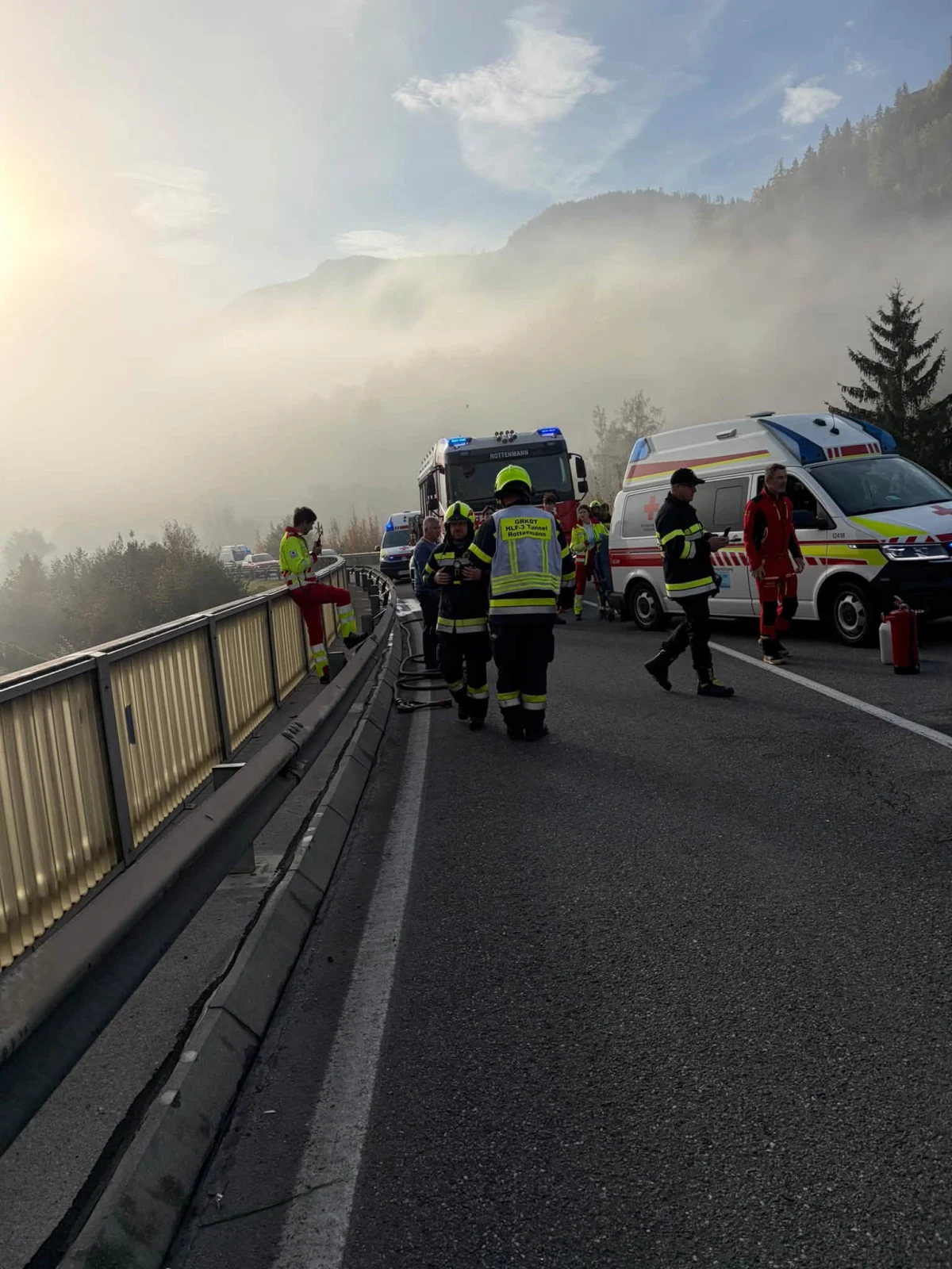 Mehrere Einsatzkräfte befinden sich auf einer nebligen Straße, umgeben von Rettungsfahrzeugen. Die Szenerie wirkt herbstlich mit dichtem Nebel im Hintergrund.
