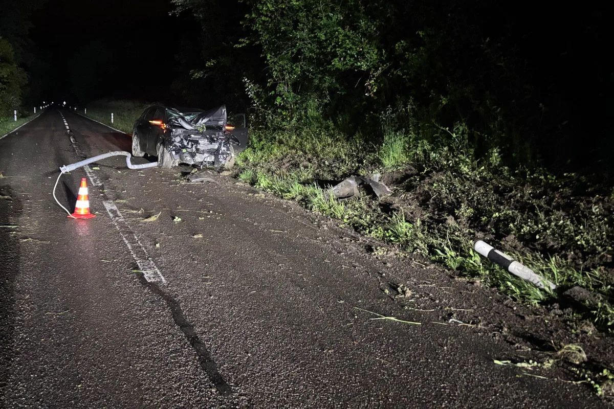 Ein stark beschädigtes Auto steht bei Nacht auf einer Landstraße. Ein Warnkegel und Trümmer sind sichtbar.