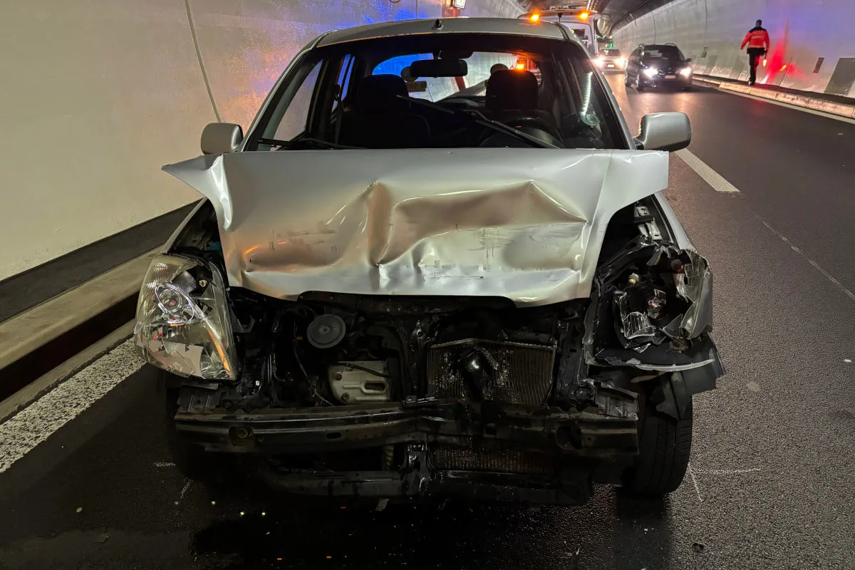 Ein Auto mit stark beschädigter Front steht in einem Tunnel. Im Hintergrund sind weitere Fahrzeuge und eine Person sichtbar.