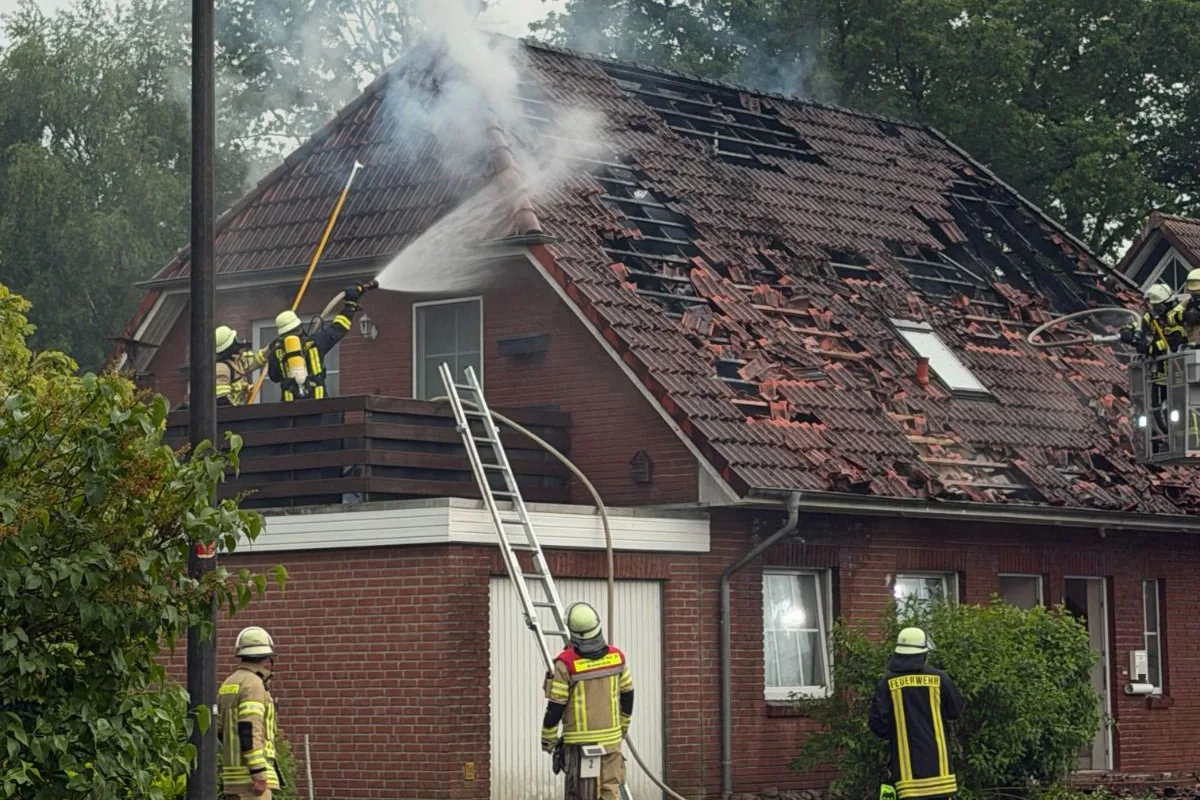 Mehrere Feuerwehrleute sind dabei, ein stark beschädigtes Hausdach zu löschen. Wasserstrahlen werden eingesetzt, um die Flammen zu kontrollieren.