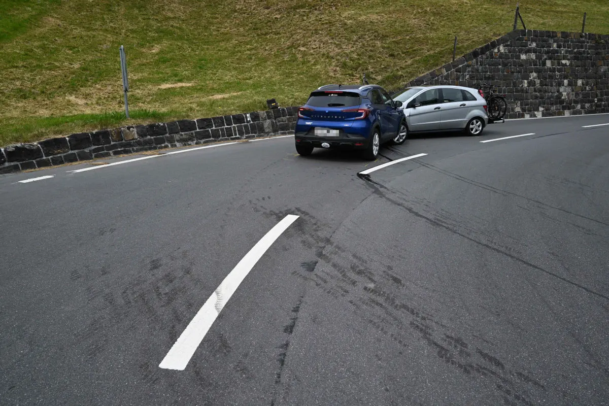 Zwei Autos sind auf einer Straße nach einem Unfall zusammengestoßen. Die Fahrzeuge stehen quer zueinander in einer Kurve und zeigen Spuren auf der Fahrbahn.