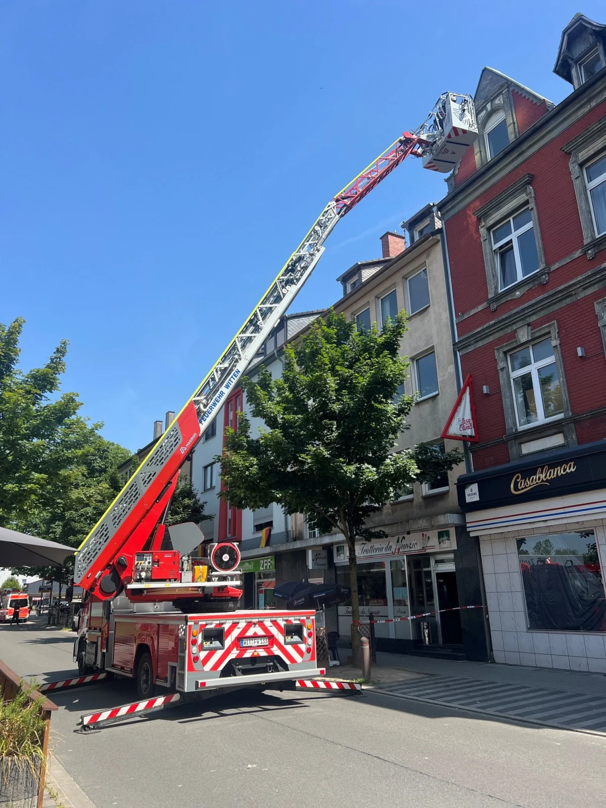 Ein Feuerwehrfahrzeug mit ausgefahrener Drehleiter steht vor einem mehrstöckigen Wohnhaus. Die Leiter reicht bis zum Dach.