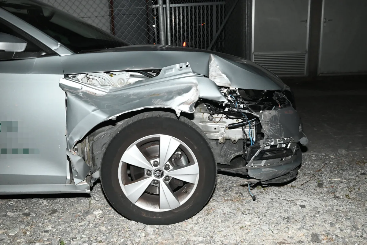 Ein silbernes Auto mit massiv eingedelltem vorderen Kotflügel und offengelegten inneren Strukturen steht auf einer Schotterfläche.