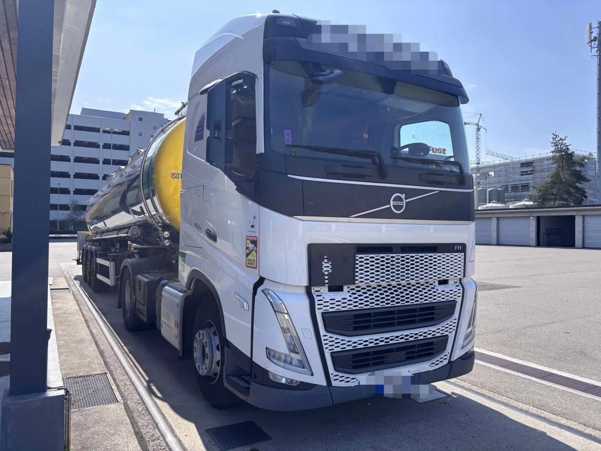 Ein weißer Volvo-Lastwagen mit Tankanhänger parkt auf einem urbanen Betriebsgelände. Im Hintergrund sind Gebäude zu sehen.