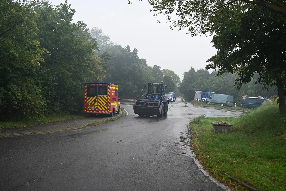 Ein Rettungswagen und ein Baufahrzeug stehen auf einer ländlichen Straße bei nebligem Wetter. Im Hintergrund sind weitere Einsatzfahrzeuge sichtbar.