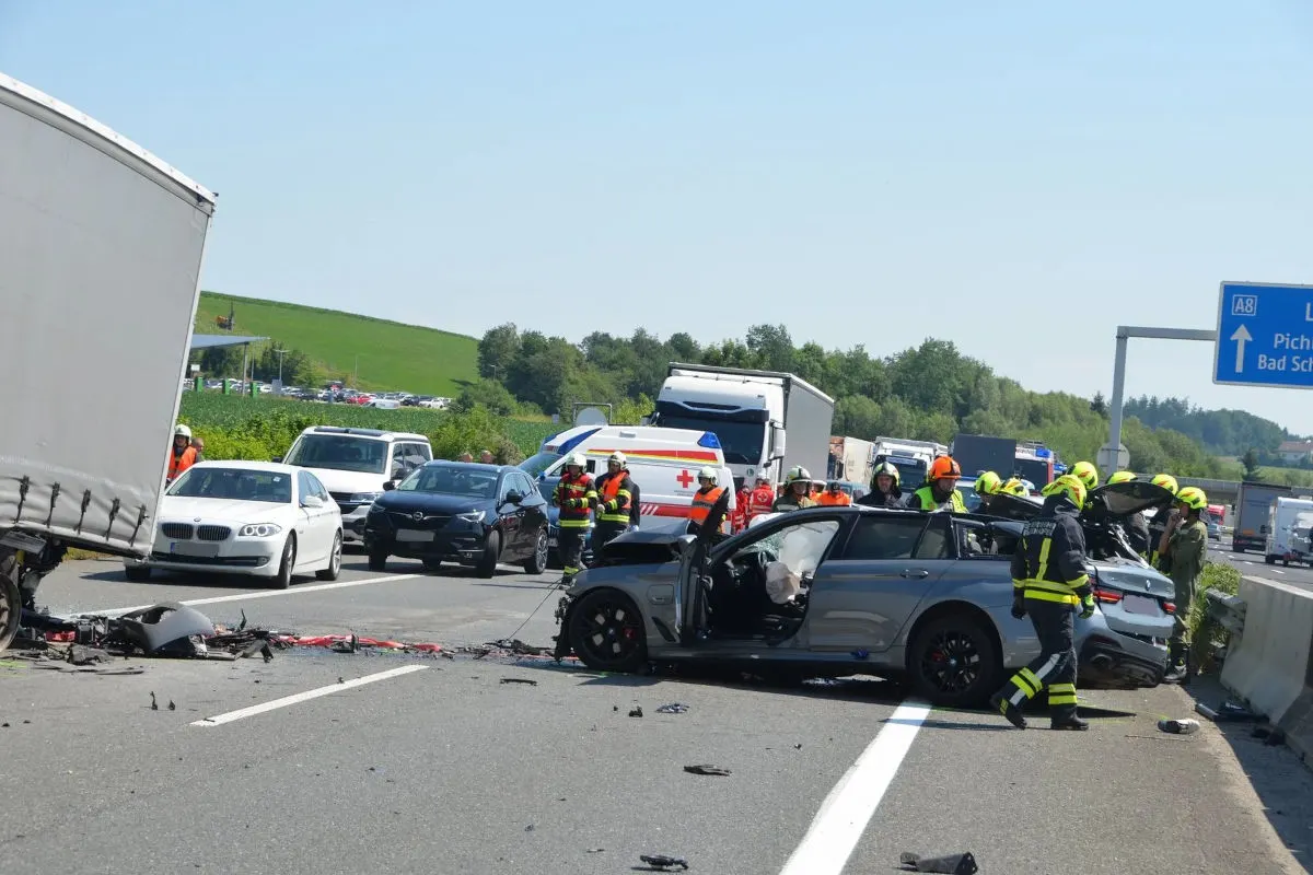 Ein schwer beschädigtes Fahrzeug steht auf der Autobahn, umgeben von Rettungskräften, während weitere Fahrzeuge im Hintergrund sichtbar sind.