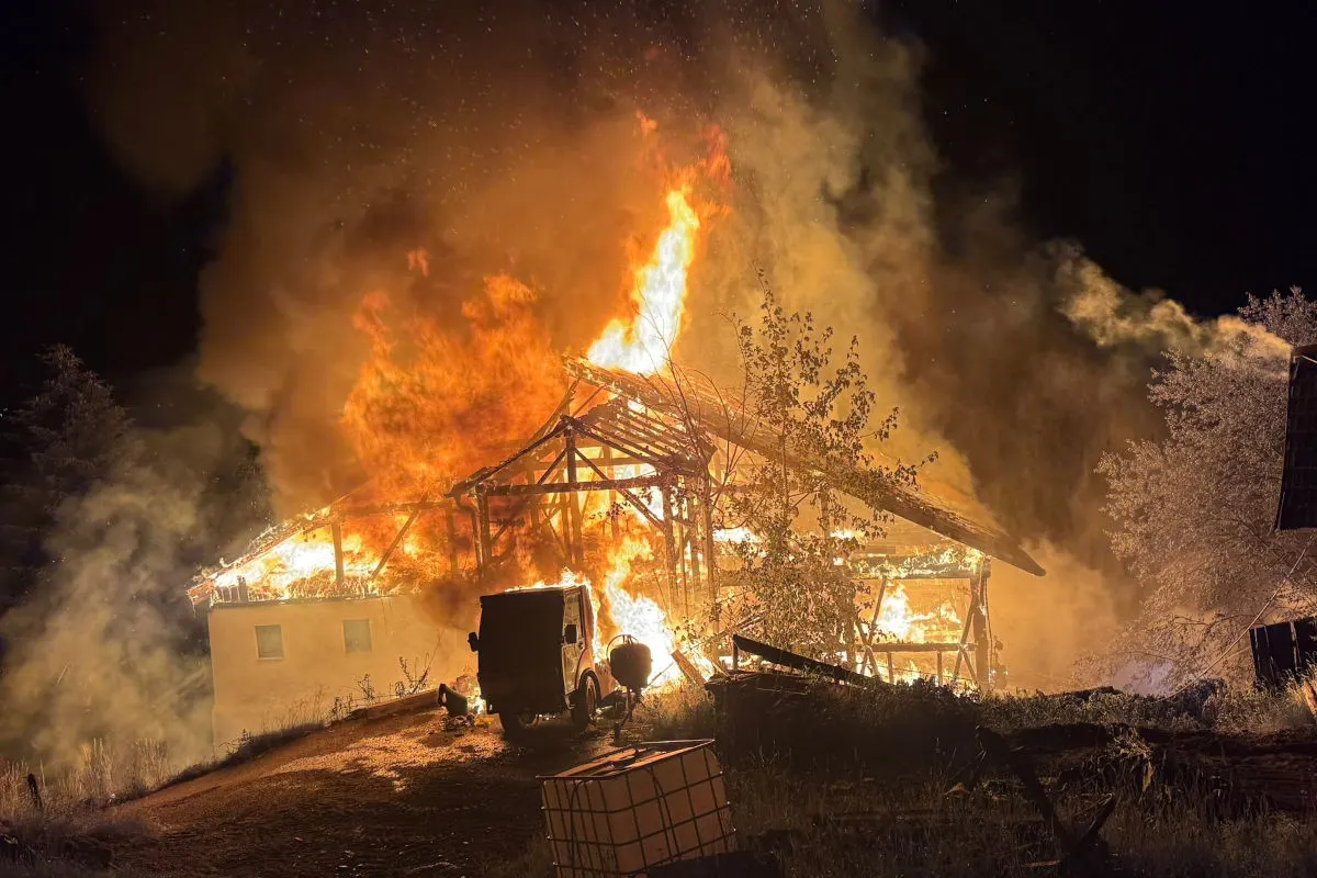 Ein Gebäude steht nachts in Flammen, wobei das Dach eingestürzt ist. Dichte Rauchwolken steigen auf, während das Feuer hell leuchtet.
