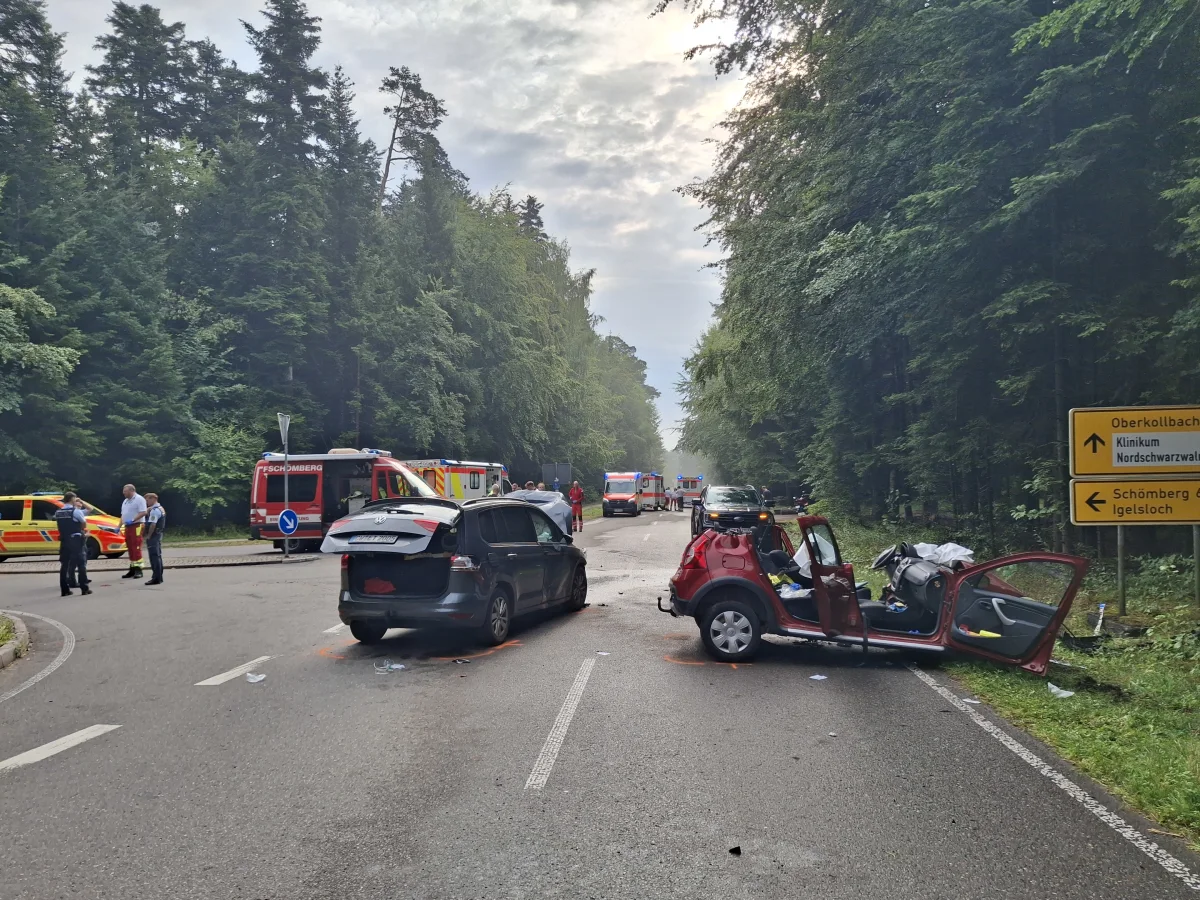 Eine Landstraße im Wald zeigt zwei beschädigte Fahrzeuge nach einem Unfall. Einsatzkräfte sind vor Ort präsent.