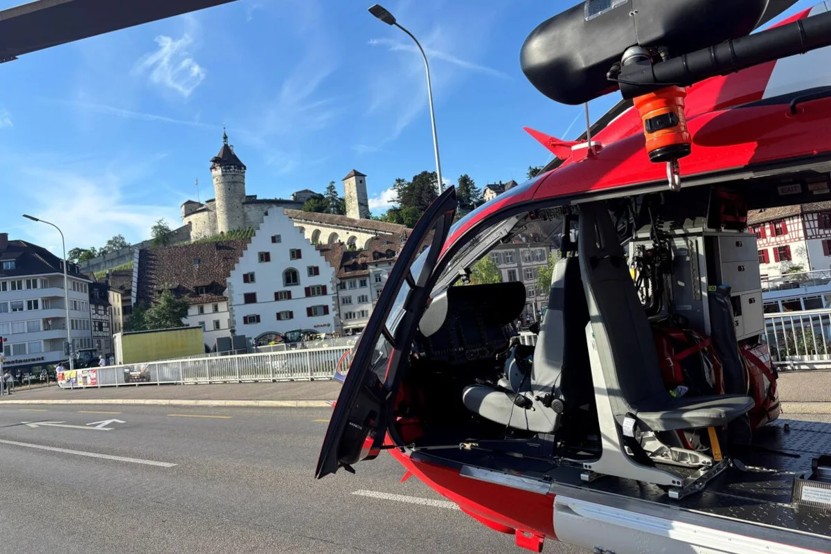 Ein geöffneter roter Rettungshubschrauber ist im Vordergrund zu sehen, während im Hintergrund historische Gebäude einer Altstadt erkennbar sind.
