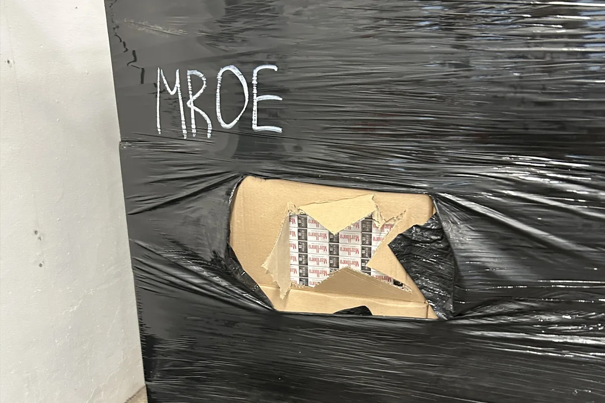 Die Aufnahme zeigt ein dicht mit schwarzer Folie umwickeltes Paket, das aufgerissen wurde. Durch die Öffnung sind mehrere Zigarettenpackungen sichtbar.