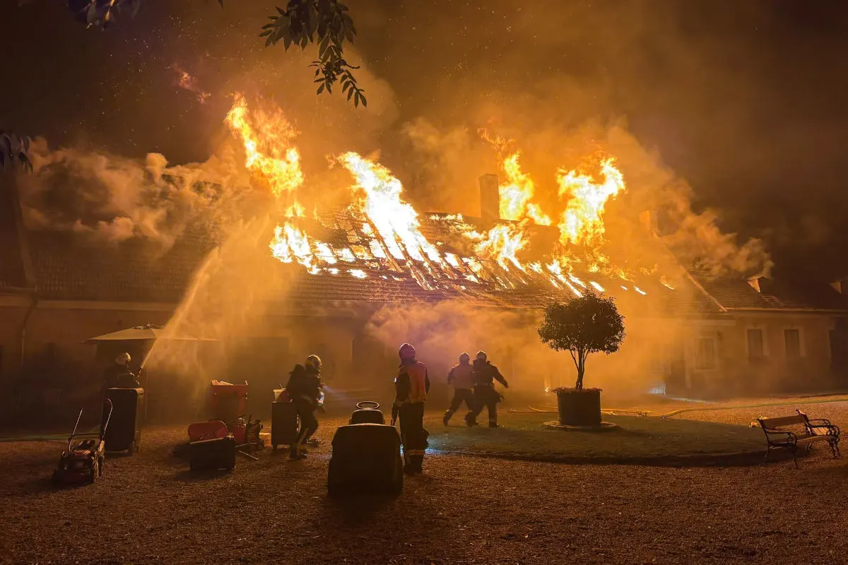 Ein brennendes Hausdach bei Nacht, umgeben von dichtem Rauch. Feuerwehrleute arbeiten an der Brandbekämpfung.