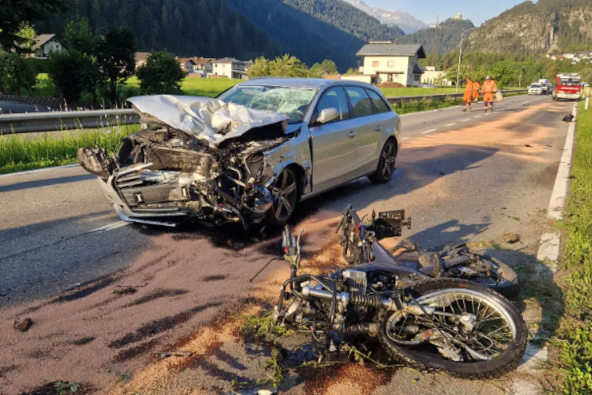 Ein silbernes Auto mit stark beschädigter Front steht auf einer Landstraße. Vor ihm liegt ein zerstörtes Motorrad.