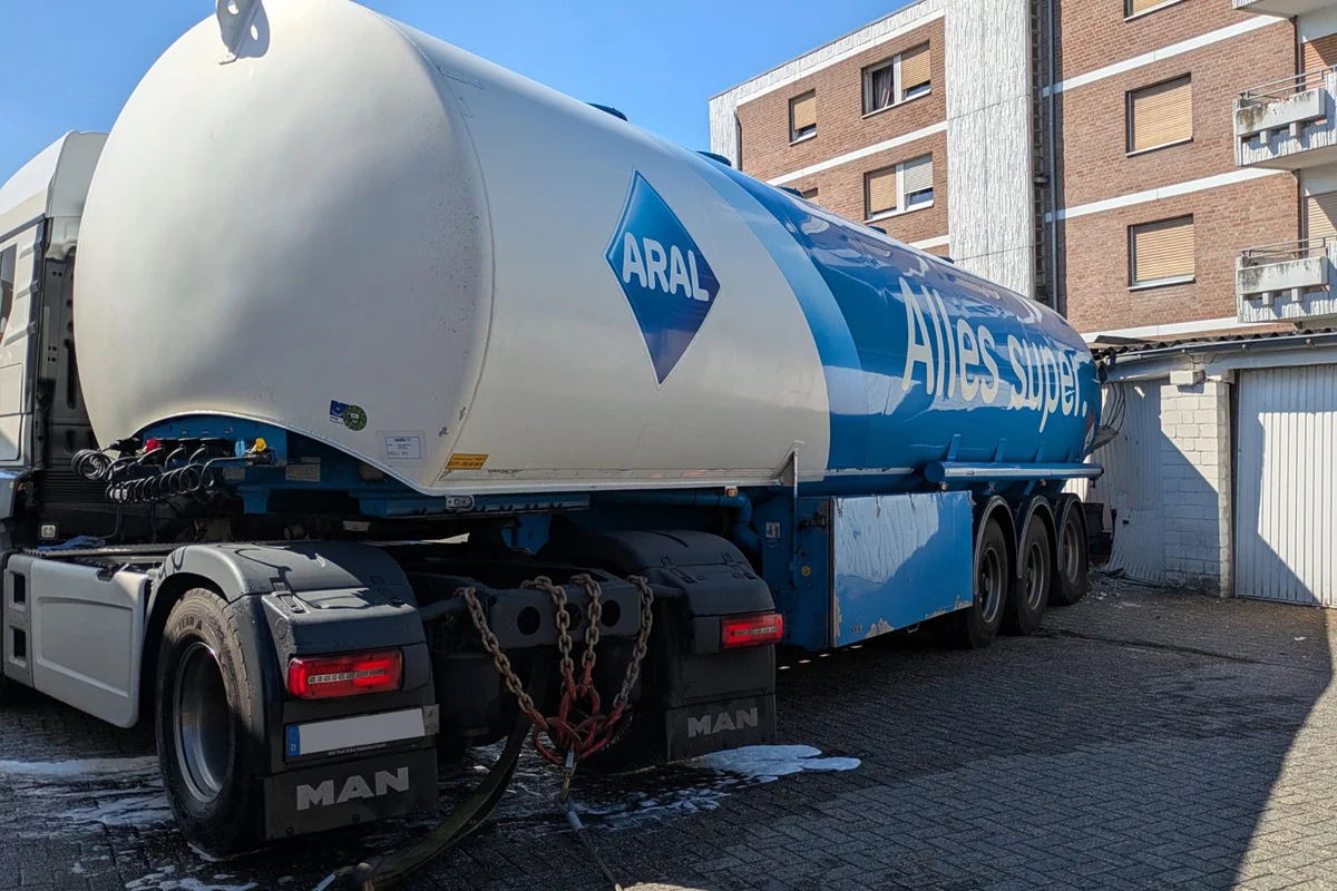 Ein ARAL-Tanklastwagen steht vor einem mehrstöckigen Wohngebäude. Der Himmel ist klar und blau.