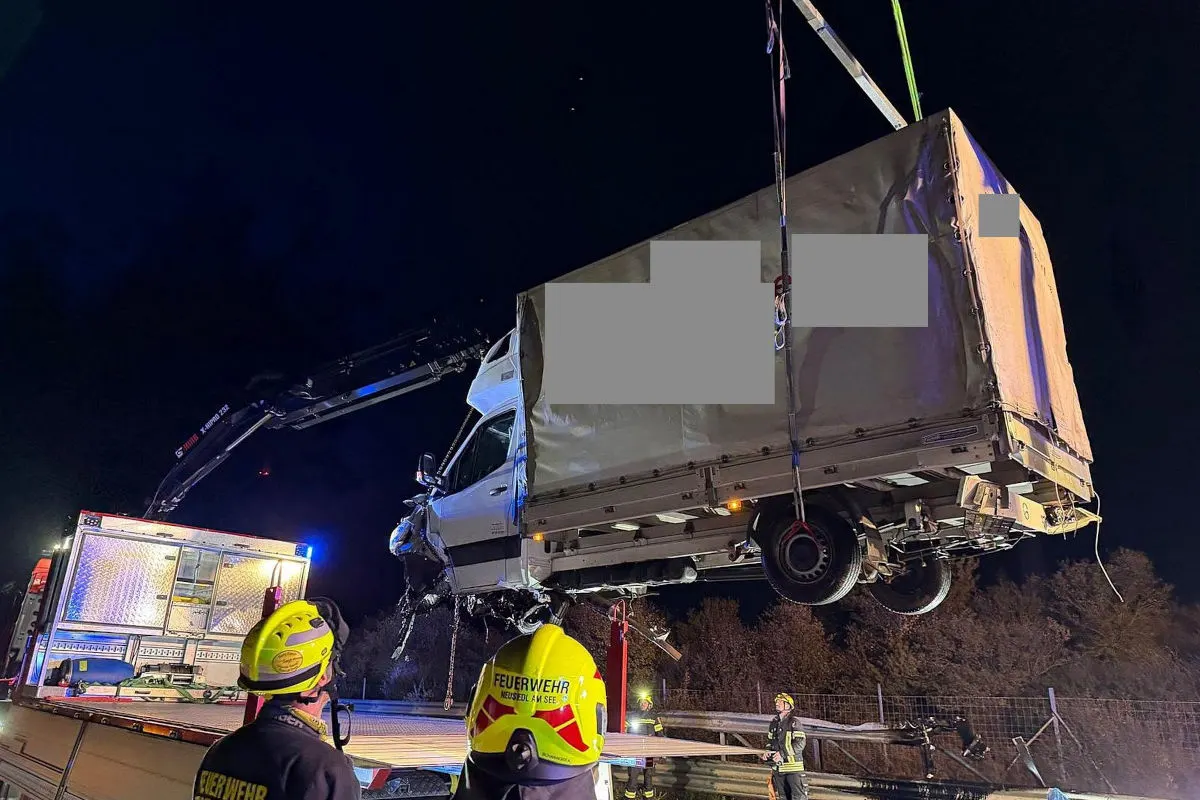 Ein Lkw wird nachts von einem Kran auf ein Abschleppfahrzeug gehoben, umgeben von Feuerwehrleuten mit Helmen.