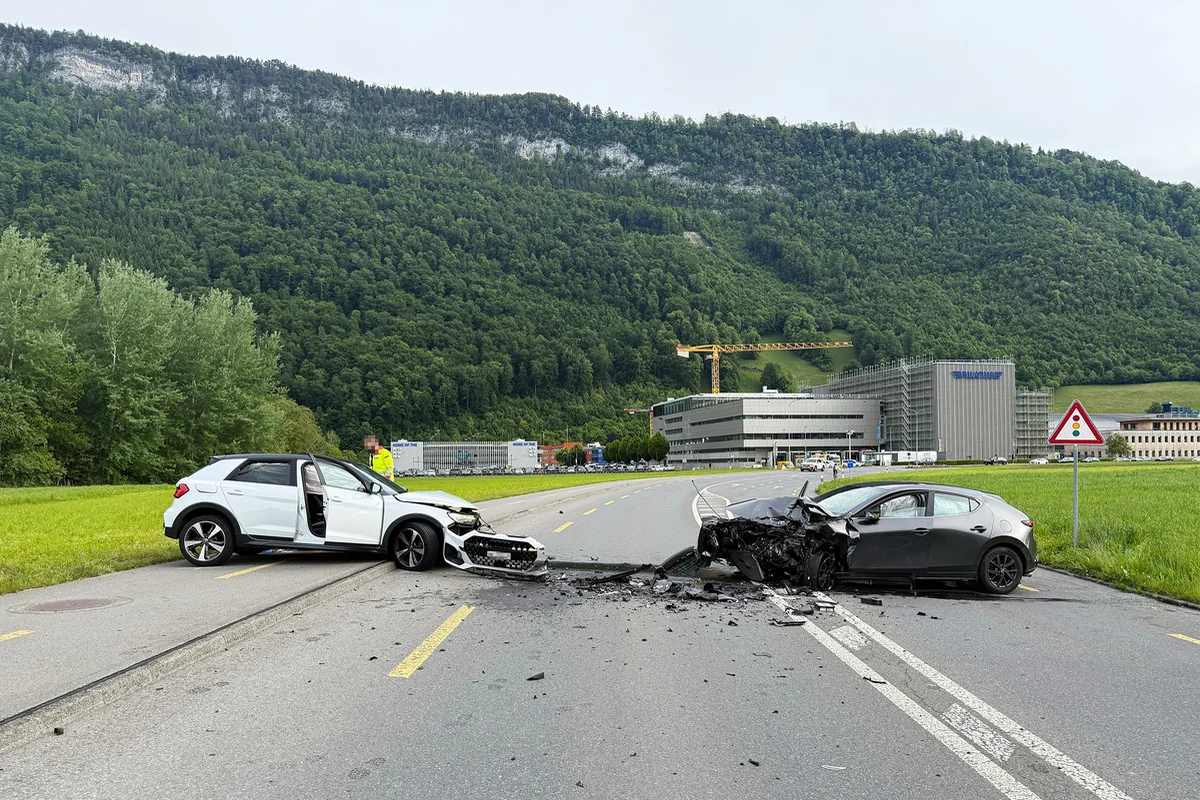 Zwei Autos kollidierten auf einer Landstraße in einer ländlichen Gegend. Beide Fahrzeuge weisen starke Frontschäden auf, während ein Mann in einer gelben Weste vor Ort ist.