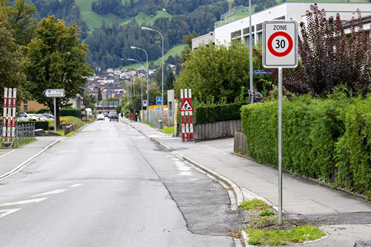 Eine gerade Straße mit Tempo-30-Verkehrsschild. Im Hintergrund sind Wohnhäuser und Vegetation zu sehen.