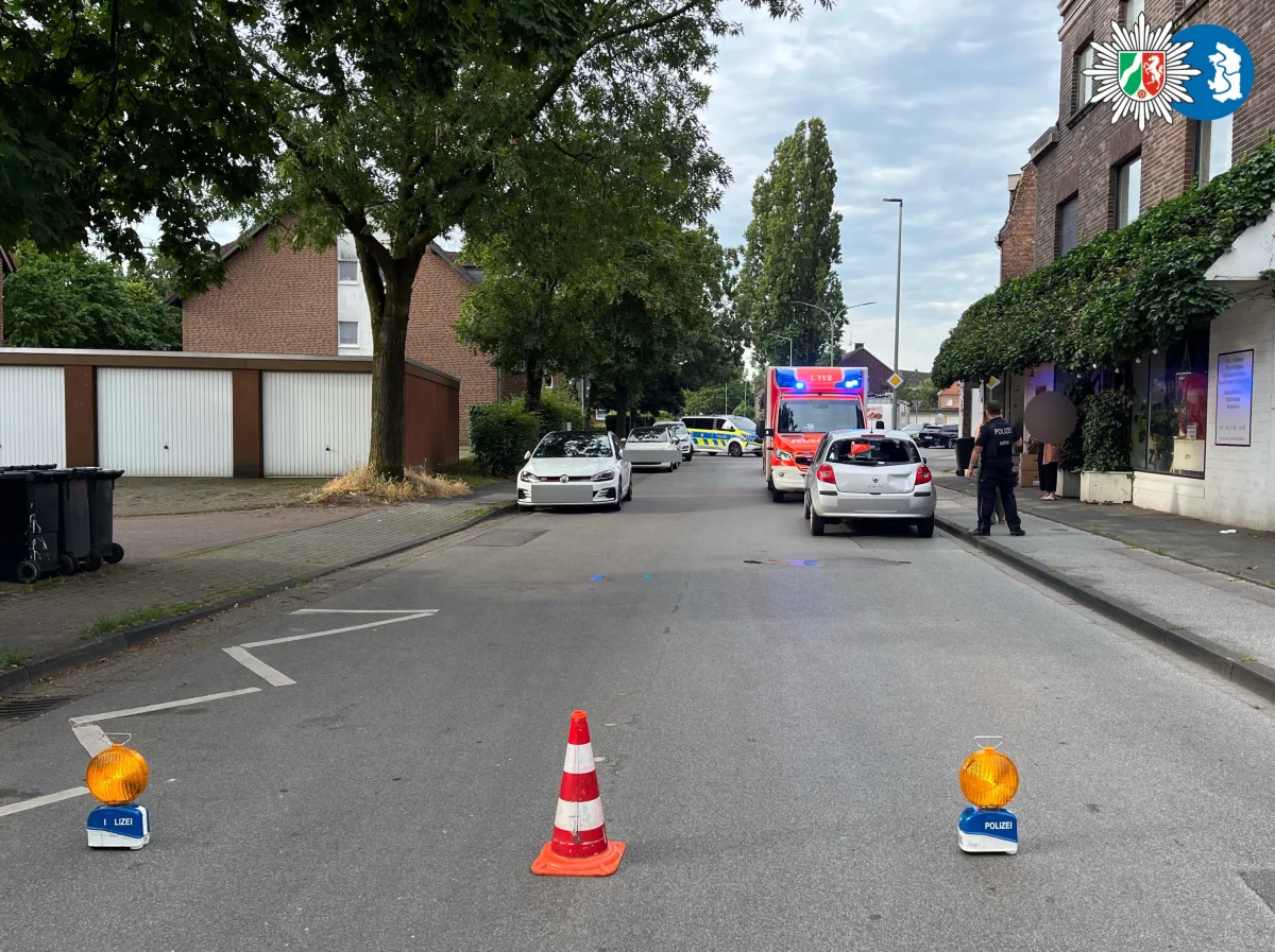 Eine städtische Straße ist abgesperrt. Polizeifahrzeuge und Beamte sind im Einsatz sichtbar.
