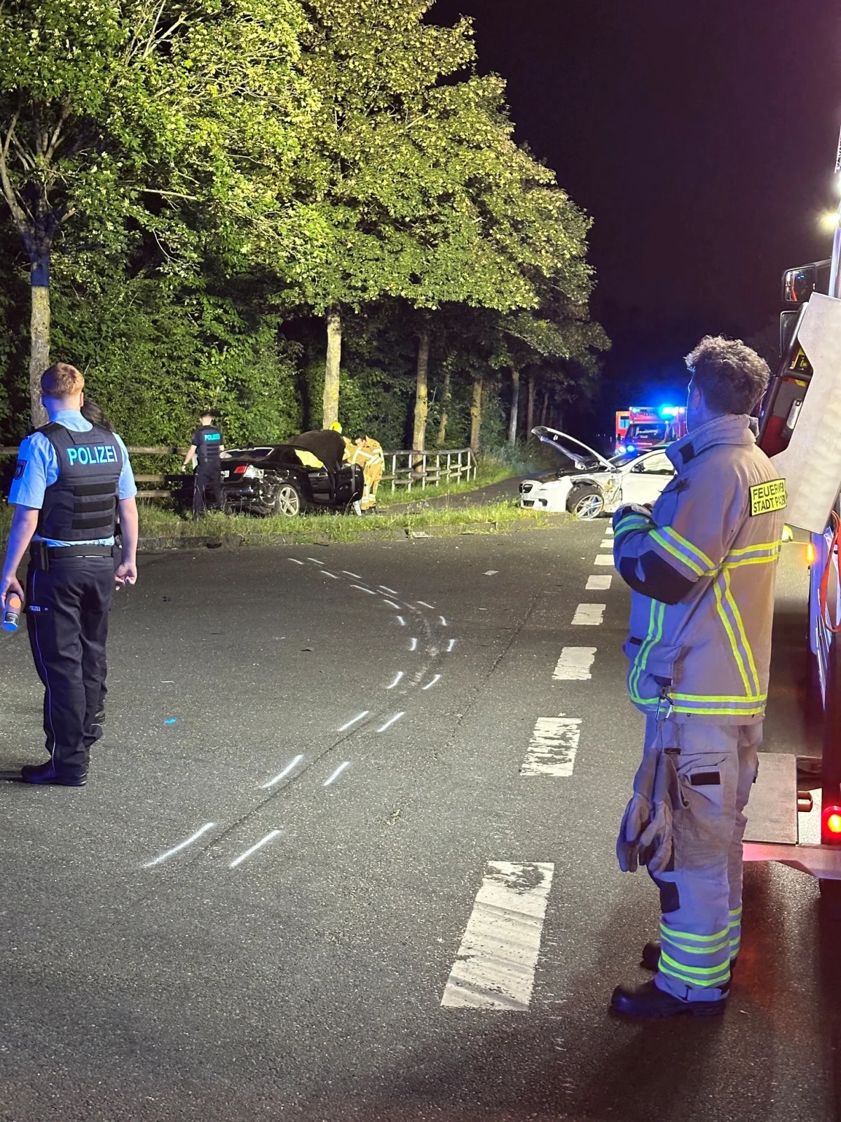Mehrere Fahrzeuge sind nach einem Unfall auf einer Landstraße bei Nacht zu sehen. Polizei und Feuerwehr sind vor Ort im Einsatz.