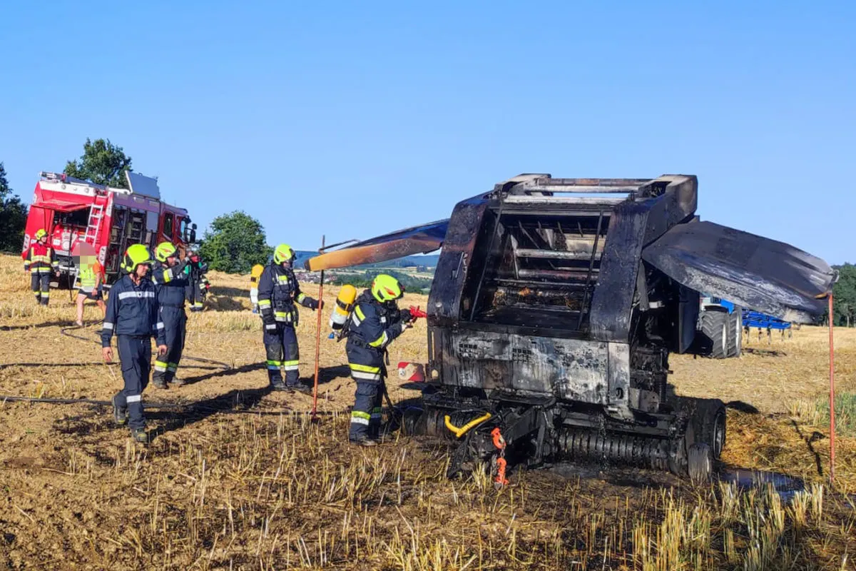 Mehrere Feuerwehrleute stehen auf einem Feld um eine verbrannte Landmaschine. Ein Feuerwehrfahrzeug ist im Hintergrund sichtbar.